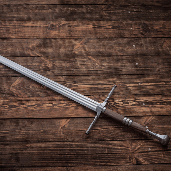 Geralt of Rivia steel sword replica in battle-ready configuration with sharp edges, historical point of balance, and 55 HRC hardness, photographed on rustic wood surface to highlight its combat-grade craftsmanship for reenactment and fantasy weapon collectors.
