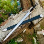 Close-up of Witcher silver sword hilt showing angular guard, leather-wrapped grip, and sculpted dragon-head pommel inspired by The Witcher 3: Wild Hunt